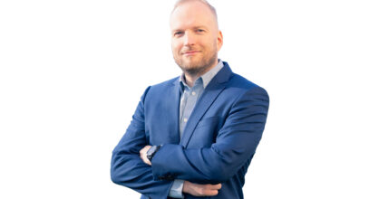 Mies hymyilee sinisessä takissa.