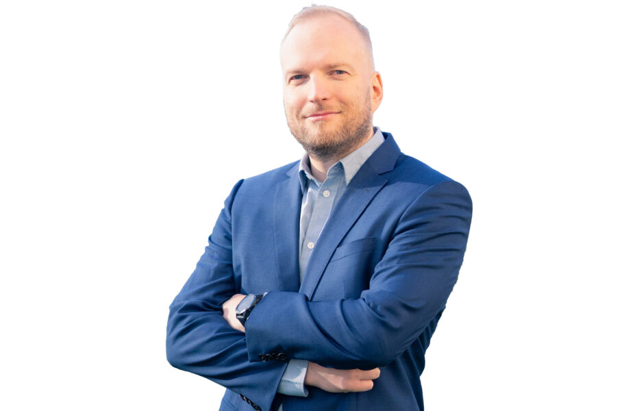 Mies hymyilee sinisessä takissa.
