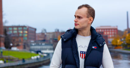 Mies katsoo kaukaisuuteen. Hänen taustallaan on koski ja rakennuksia.