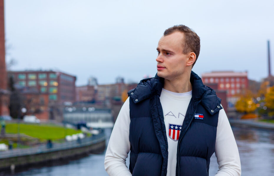 Mies katsoo kaukaisuuteen. Hänen taustallaan on koski ja rakennuksia.