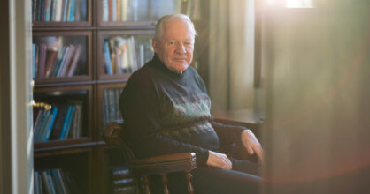 Mies istuu mukavannäköisessä tuolissa ja hymyilee.