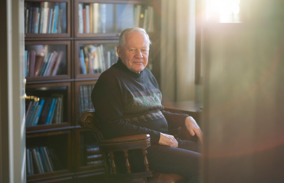 Mies istuu mukavannäköisessä tuolissa ja hymyilee.