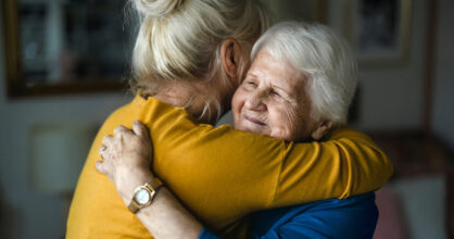 Aikuinen keski-ikäinen nainen halaa iäkästä naista.