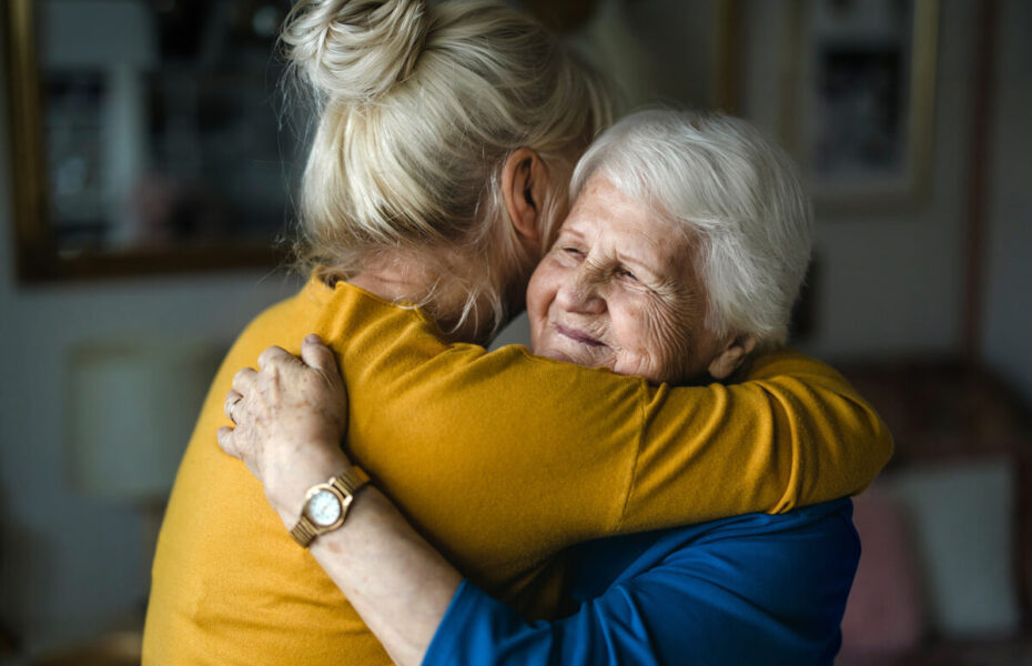Aikuinen keski-ikäinen nainen halaa iäkästä naista.