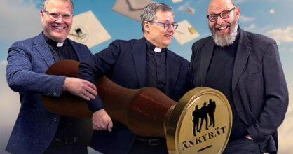 Kolme miestä hymyilee. He pitävät sylissään sinetti, jossa lukee "änkyrät".