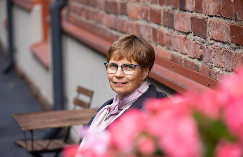 Annamari Jukko istuu pöydän ääressä ulkona. Hänellä on lyhyet hiukset ja silmälasit.