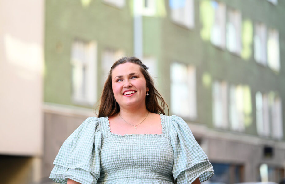Anni Niskanen seisoo kerrostalon edustalla ja katselee kohti taivasta.