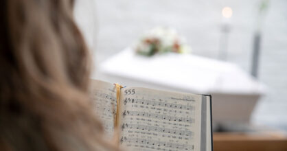 Henkilö lukee virsikirjaa. Taustalla näkyy hauta-arkku.