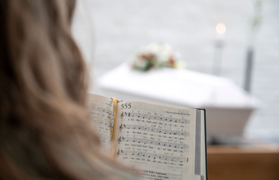 Henkilö lukee virsikirjaa. Taustalla näkyy hauta-arkku.