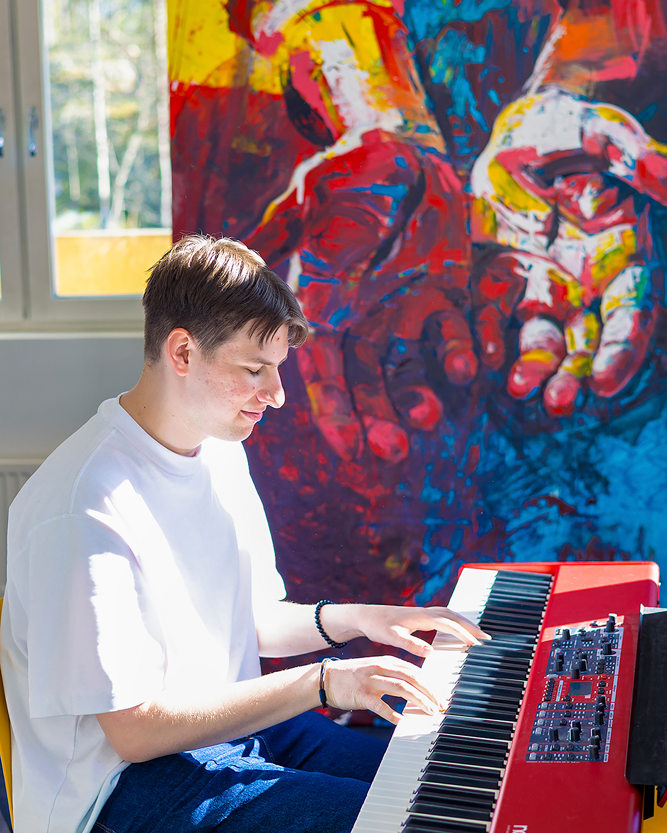 Mies soittaa pianoa ja hymyilee. Hänen taustallaan on maalaus, jossa on Jeesuksen lävistetyt kädet.