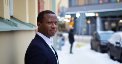 Chima Igwe seisoo kerrostalon seinää vasten.