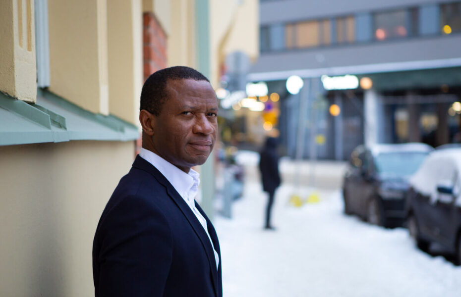 Chima Igwe seisoo kerrostalon seinää vasten.