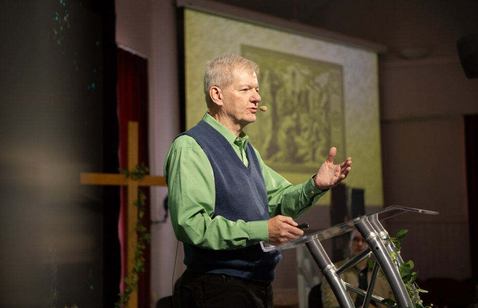 Mies vihreässä kauluspaidassa ja harmaassa liivissä puhujapöntön takana.