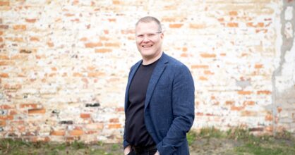 mies pikkutakissa ja kädet taskussa hymyilee
