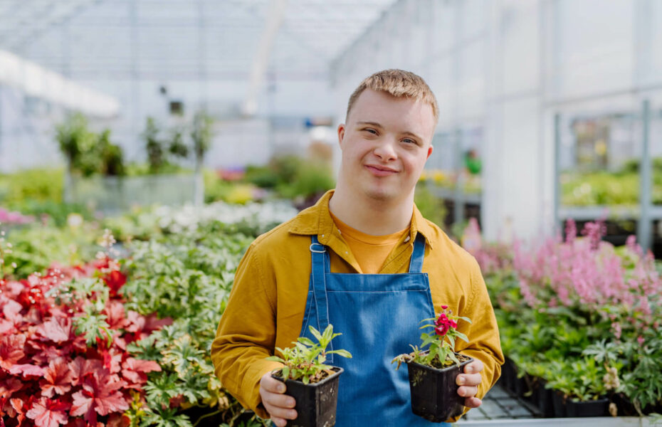 Down-mies pitää käsissään kahta kukkapurkkia kasvihuoneessa.