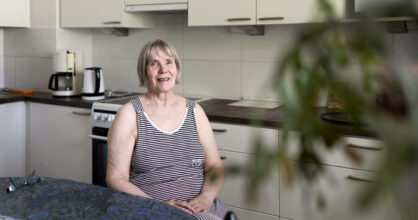 Kuvassa Eeva Piiroinen istuu keittiön pöytänsä ääressä ja hymyilee.