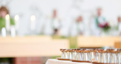 Kirkon alttarilla on rivissä hopeisia maljoja, taustalla hämärästi näkyviä henkilöitä vihreissä vaatteissa.