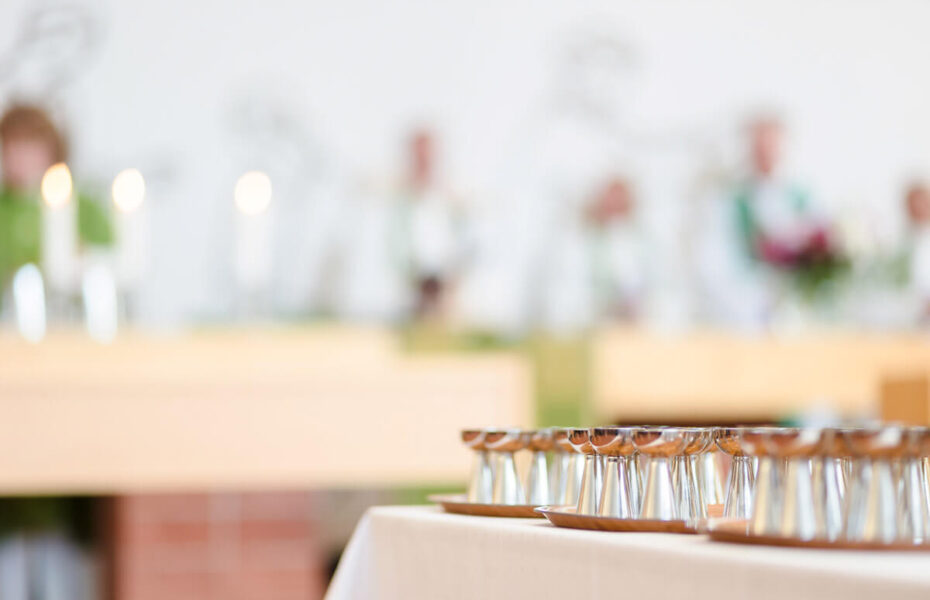 Kirkon alttarilla on rivissä hopeisia maljoja, taustalla hämärästi näkyviä henkilöitä vihreissä vaatteissa.