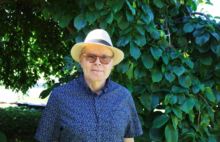 Georg Ahnen seisoo pensaan varjossa aurinkoisena päivänä. Hänellä on aurinkolasit ja aurinkohattu.