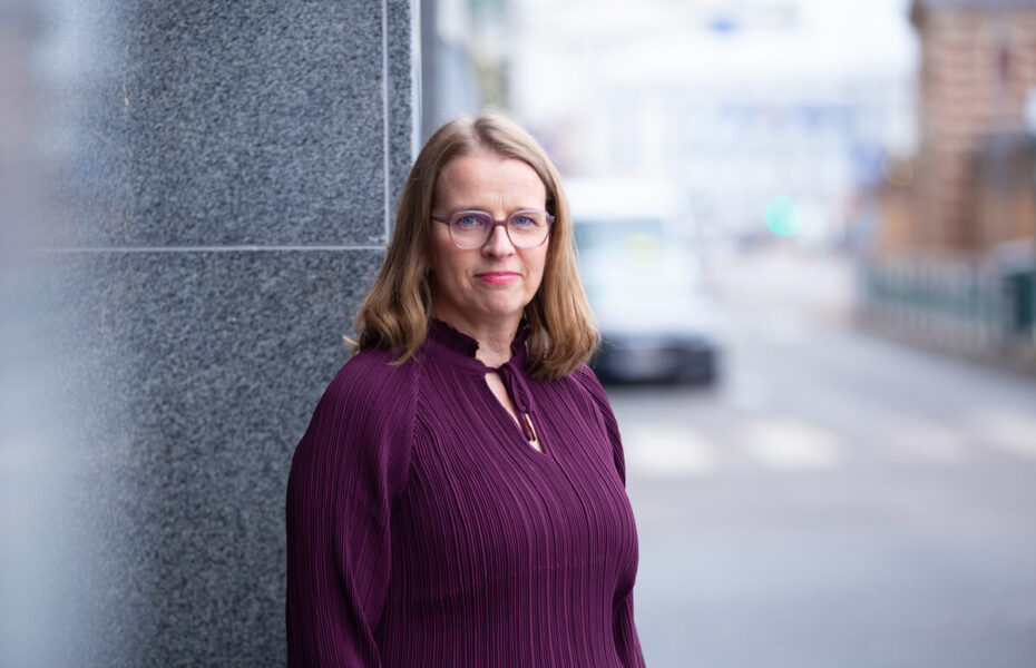 Hanna Salomäki hymyilee. Hänellä on silmälasit ja violetti paita sekä hartioille asti ulottuvat hiukset.