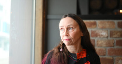 Keski-ikäinen nainen katsoo ikkunasta ulos. Hänellä on pitkät ruskeat hiukset, joiden latvat on värjätty violetiksi.