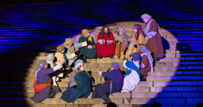 Jeesus istuu portailla seuraajiensa kanssa. Heidät on ympäröinyt valokeila.