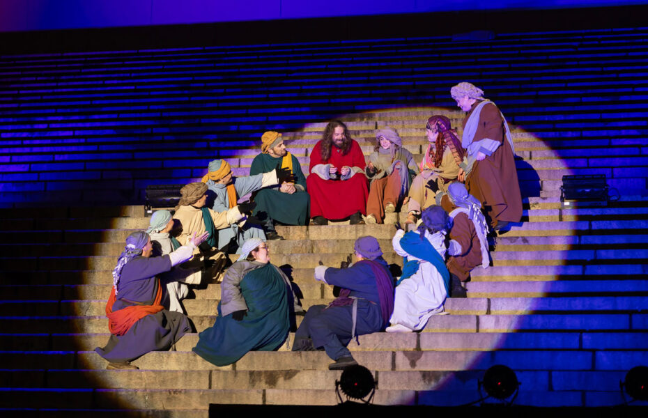 Jeesus istuu portailla seuraajiensa kanssa. Heidät on ympäröinyt valokeila.