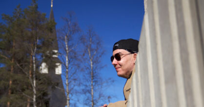 Aurinkolasipäinen mies nojaa betoniaitaan.