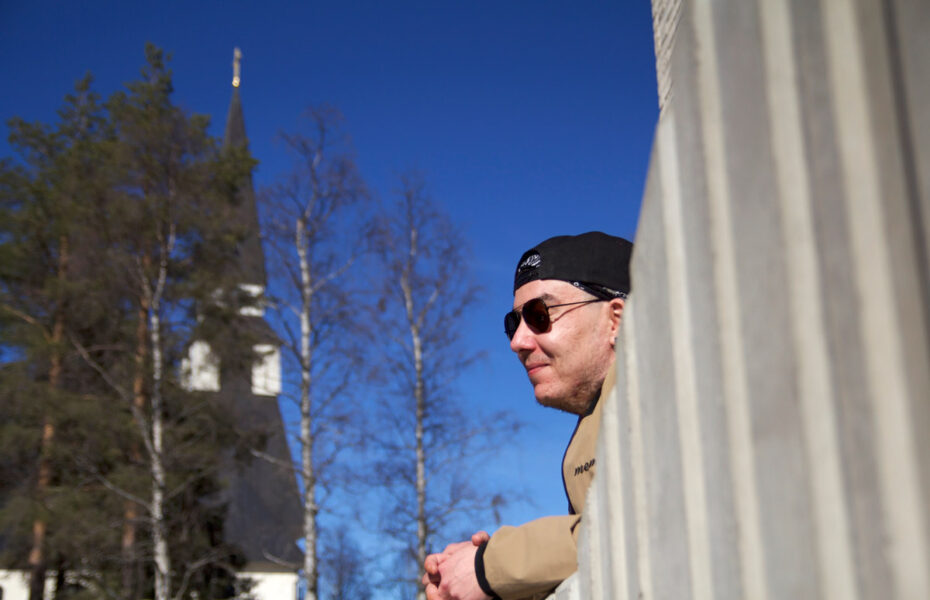 Aurinkolasipäinen mies nojaa betoniaitaan.
