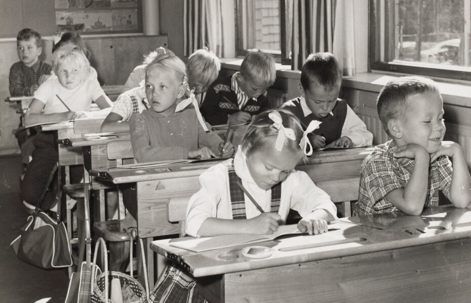 Mustavalkoinen kuva kansakoulun oppilaista pulpeteissaan.