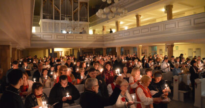 Joukko ihmisiä kirkkorakennuksen sisällä kynttilä kädessä.