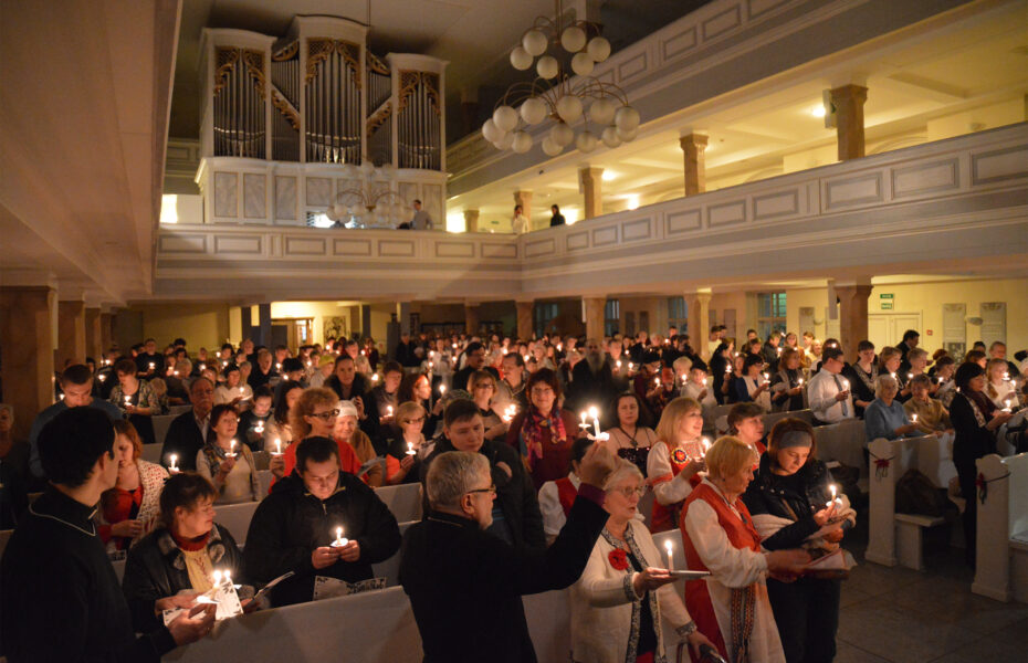 Joukko ihmisiä kirkkorakennuksen sisällä kynttilä kädessä.