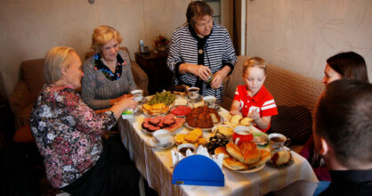 Mummoja ja pikkupoika pöydän ympärillä. Pöydässä on paljon ruokaa ja herkkuja.