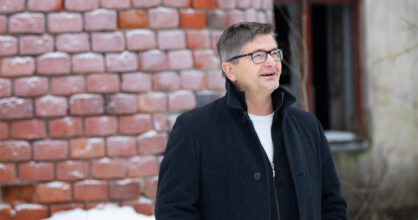 mustahiuksinen mies naurahtaa ulkona. Takana lunta.