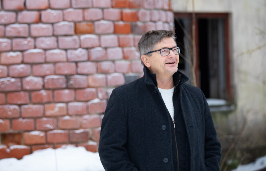 mustahiuksinen mies naurahtaa ulkona. Takana lunta.