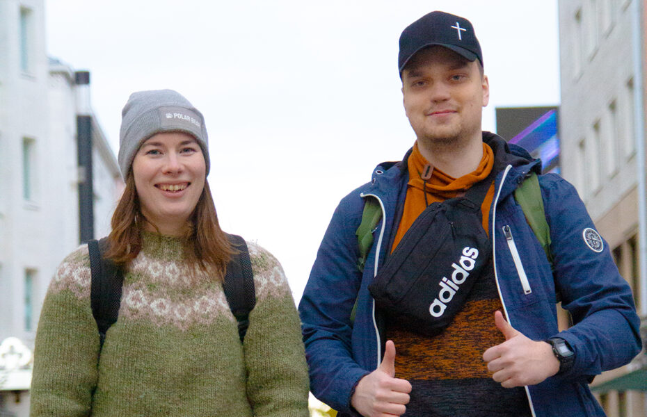 Nainen ja mies hymyilee kaupungin kadulla. Miehellä on peukalot pystyssä.