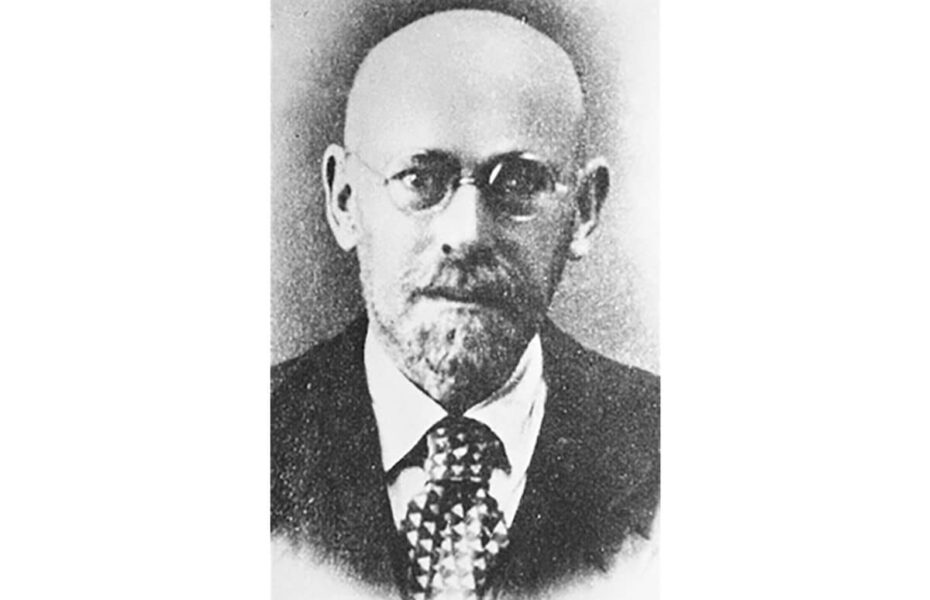 Mustavalkoinen kuva miehestä, joka on kalju ja jolla on silmälasit.