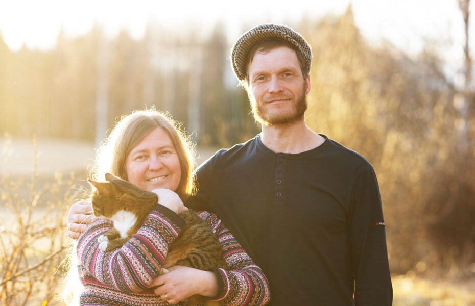 Aurinko kajastaa naisen ja miehen takaa. Naisen sylissä on kissa.