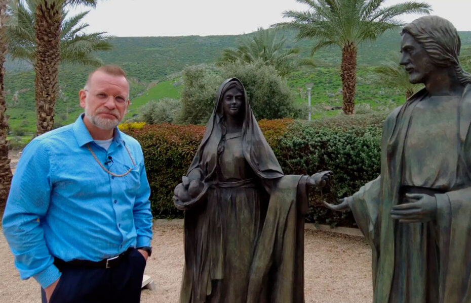 Siniseen kauluspaitaan pukeutunut mies seisoo kahden patsaan vieressä.