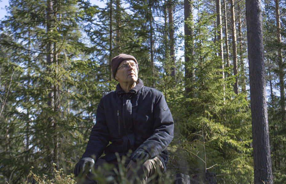 Jarmo Laitinen istuu metsässä. Hänellä on lämpimät vaatteet, ja hän katsoo yläviistoon.