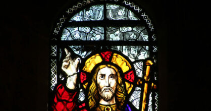 Jeesus-lasimaalaus ikkunassa. Jeesus osoittaa sormellaan kohti taivasta.