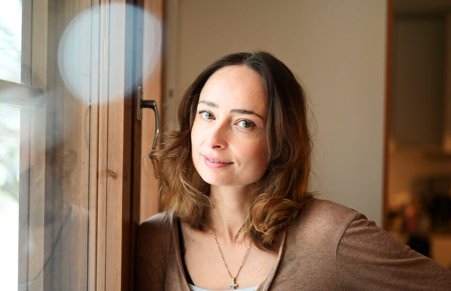 Joanna Vähäsarja nojaa ikkunaan. Hänellä on hartioille asti ulottuvat lainehtivat hiukset.