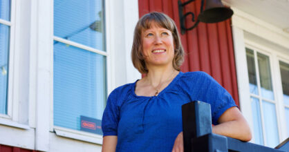 Johanna Sandberg nojaa portaan kaiteeseen ja katsoo kaukaisuuteen. Hänellä on polkkahiukset ja sininen paita.