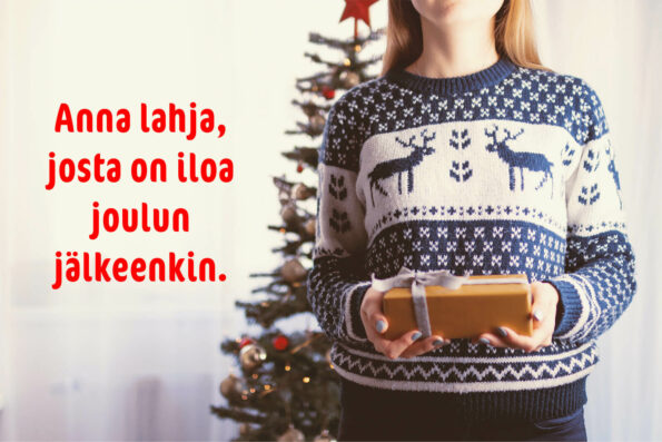 Villapaitaan pukeutunut nainen pitää käsissään lahjapakettia. Hänen takanaan on joulukuusi. Kuva on teksti: Anna lahja, josta on iloa joulunkin jälkeen.