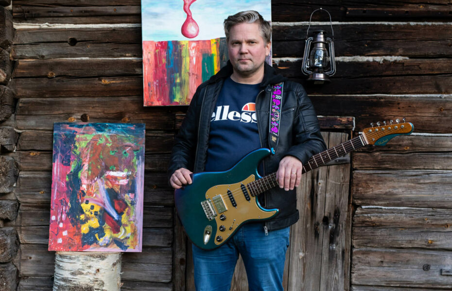 JP Löfberg seisoo kitaran kanssa hirsiseinän edessä.