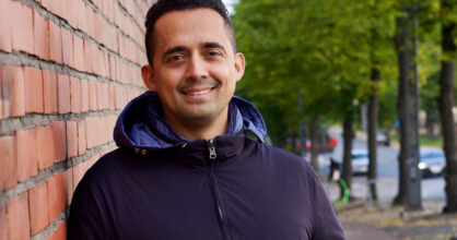 mies hymyilee ja nojaa tiiliseinään.