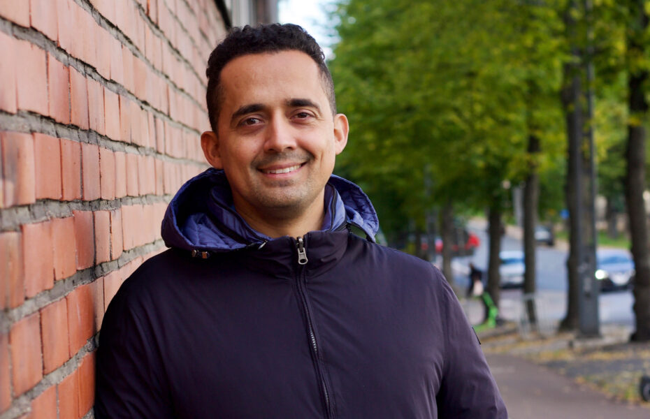 mies hymyilee ja nojaa tiiliseinään.