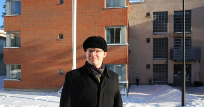 Mies on ulkona. Hänellä on musta lakki ja takki.