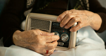 Iäkkään naiset kädet säätävät radiota.