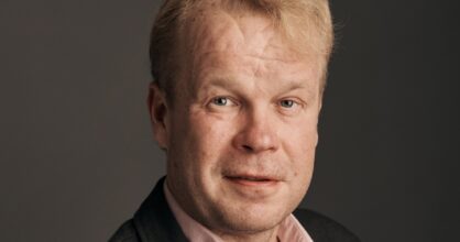 Mies kauluspaidassa ja pikkutakissa. Lähikuva kasvoista.